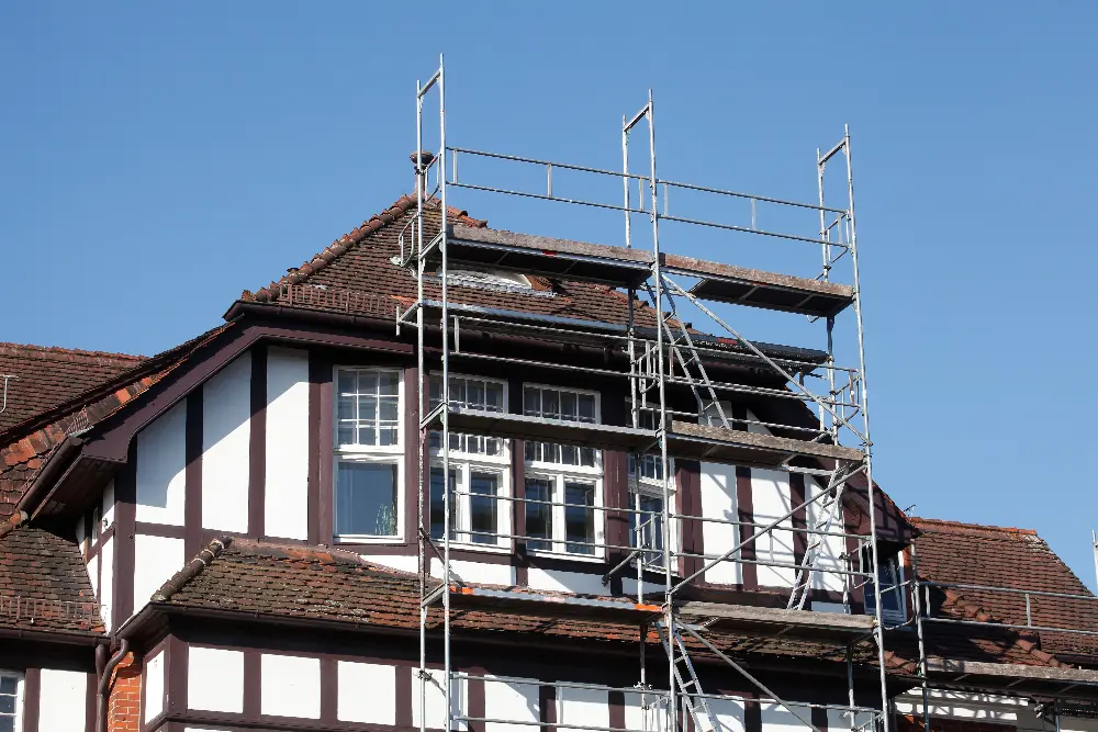Ein Gerüst für die Sanierung der Außenfassade steht vor einem klassischen weißen Fachwerkhaus